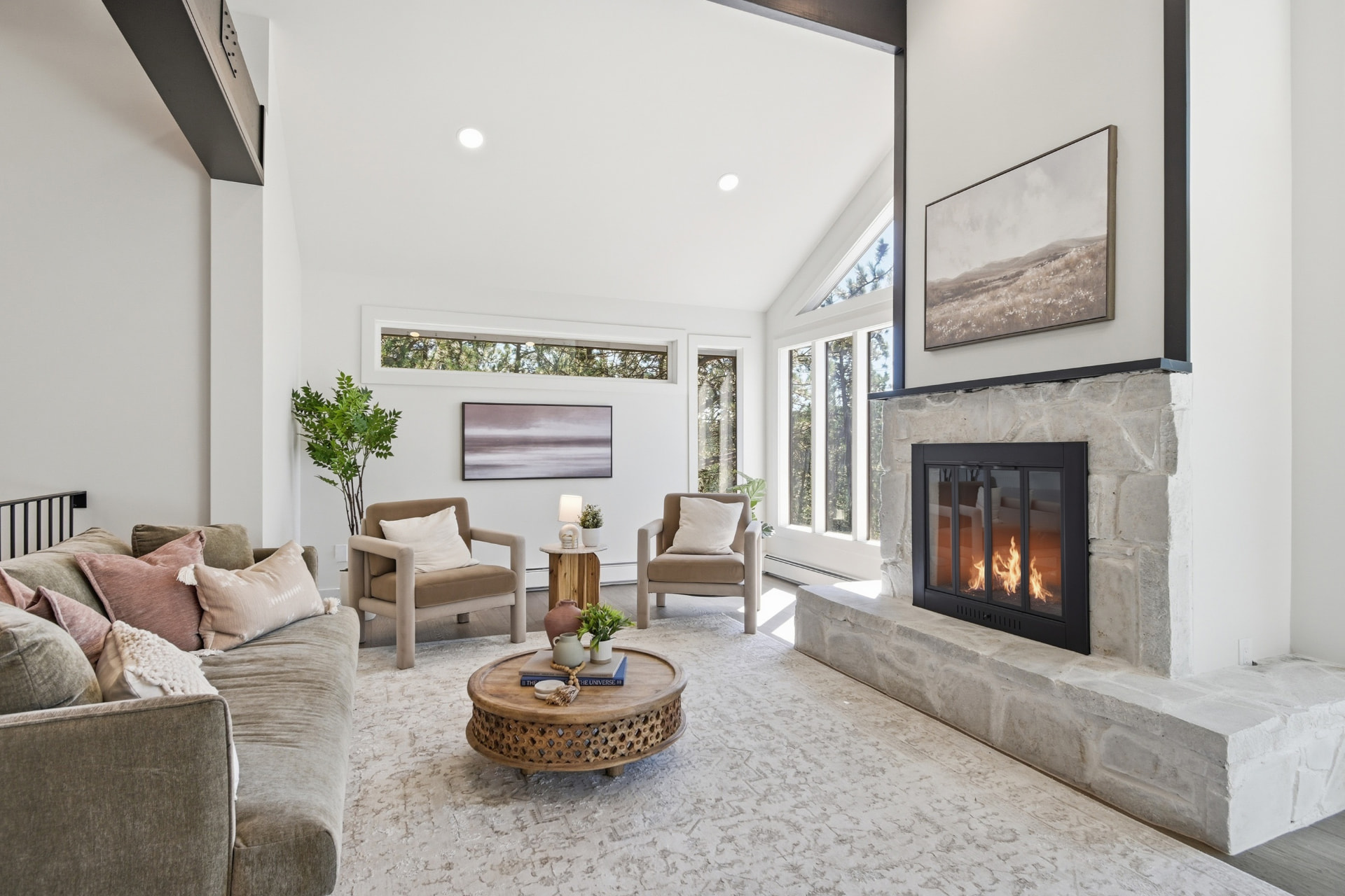 Living room with a lit stone fireplace, a gray-green sofa, and a carved wooden coffee table