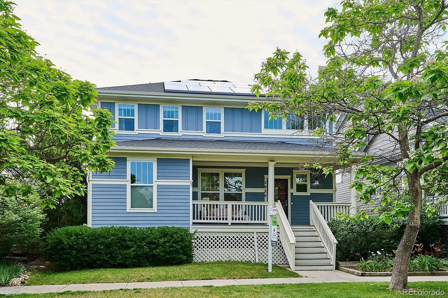 Blue two-story home with a covered front porch and rooftop solar panels
