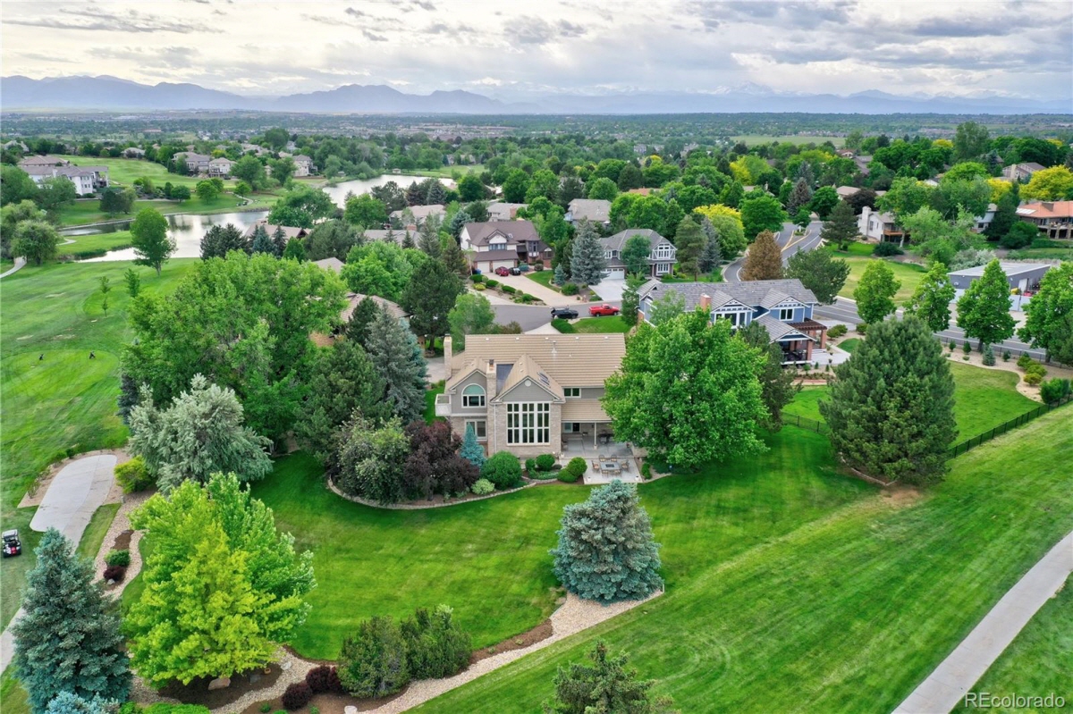 Aerial view of a large two-story home beside a golf course with mountains on the horizon