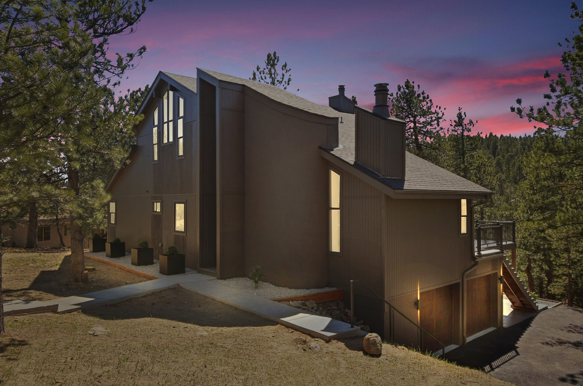 Mountain home at dusk with warm interior lights beneath a colorful sky