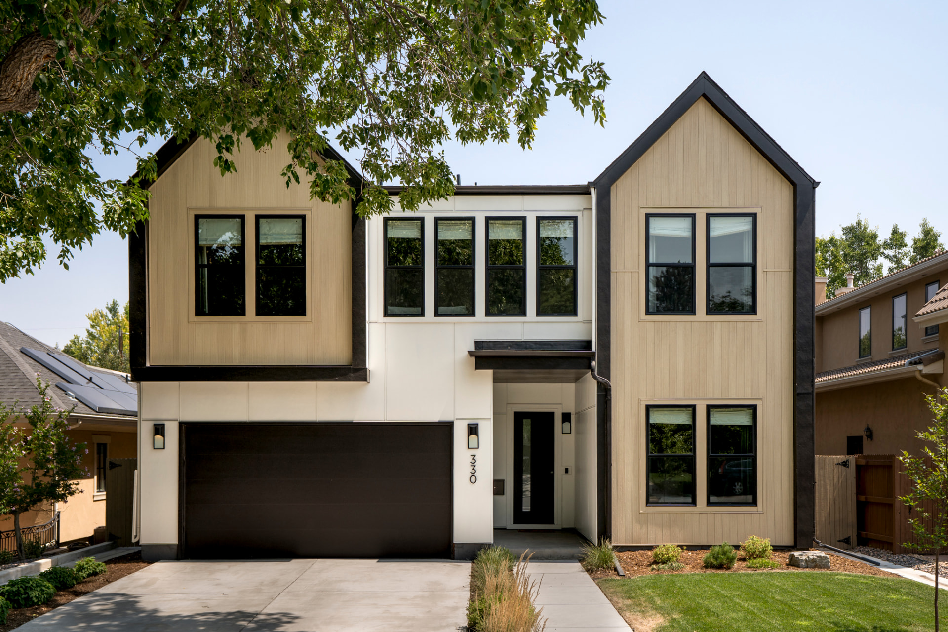 Modern two-story home with tan siding, dark trim, and a gabled roofline